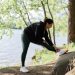 A woman in sportswear stretches by a serene lake surrounded by trees, embracing nature and fitness.